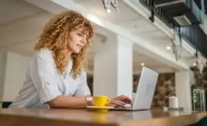 Woman with curly hair sits at a desk with a laptop in front of her