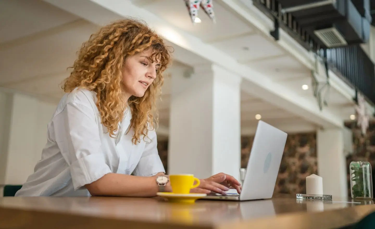 Woman with curly hair sits at a desk with a laptop in front of her